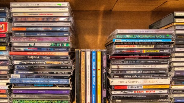 Stack of CDs in cases on a wooden shelf, evoking the early-2000s era of CD ripping and file sharing